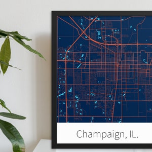 May include: A framed map of Champaign, Illinois, with a dark blue background and orange lines representing streets. The city name is printed in white at the bottom of the map.