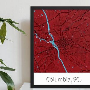 May include: A framed map of Columbia, South Carolina, with a red background and blue river. The city streets are shown in black lines. The text "Columbia, SC." is printed below the map.