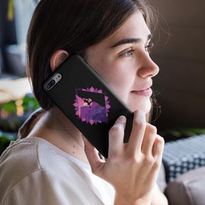 May include: Black phone case with a geometric design in shades of purple and pink. The case is held up to the ear, showcasing the design's intricate details. The phone case is a sleek accessory.
