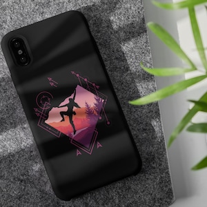 May include: Black phone case featuring a geometric design with a silhouette of a rock climber against a sunset backdrop. The design includes pink, purple, and orange hues, with geometric shapes and arrows. The case is on a gray surface.