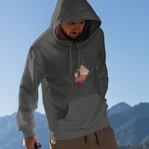 May include: A dark gray hooded sweatshirt with a graphic design of a person climbing a mountain with a sunset in the background. The design is surrounded by geometric shapes.