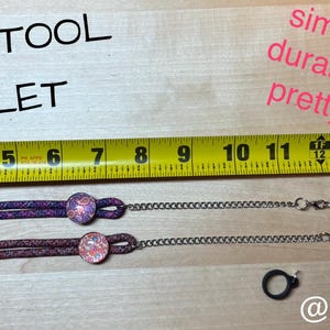 May include: Two purple and pink braided wristlets with silver chains and black metal clasps. The wristlets are measured on a tape measure with the words "THE LOC TOOL WRISTLET" above the tape measure. The words "simple durable pretty" are written in pink above the tape measure. The words "@jameica.perez" are written below the tape measure.