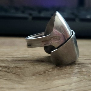 K&ouml;nnte beinhalten: Ein silberner Ring mit einem einzigartigen, eckigen Design. Der Ring besteht aus zwei Teilen, die ineinandergreifen und eine spitze, geometrische Form bilden.