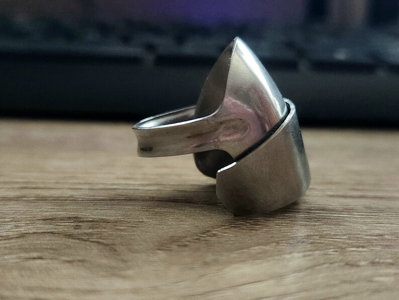 K&ouml;nnte beinhalten: Ein silberner Ring mit einem einzigartigen, eckigen Design. Der Ring besteht aus zwei Teilen, die ineinandergreifen und eine spitze, geometrische Form bilden.