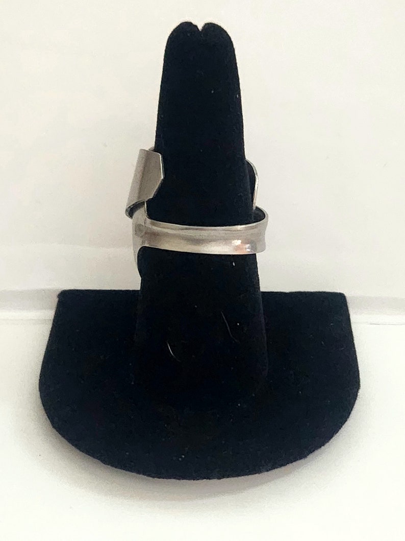 K&ouml;nnte beinhalten: Ein silberner Ring mit einem einzigartigen, offenen Design. Der Ring wird auf einem schwarzen Ringst&auml;nder pr&auml;sentiert.
