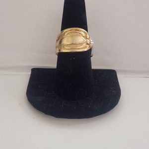 Puede incluir: Un anillo de color dorado con un diseño decorativo en un soporte de anillo negro.