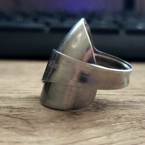 K&ouml;nnte beinhalten: Ein silberner Ring aus einem verbogenen L&ouml;ffel. Der Ring ist oval geformt und hat ein Band, das sich um den Finger legt.