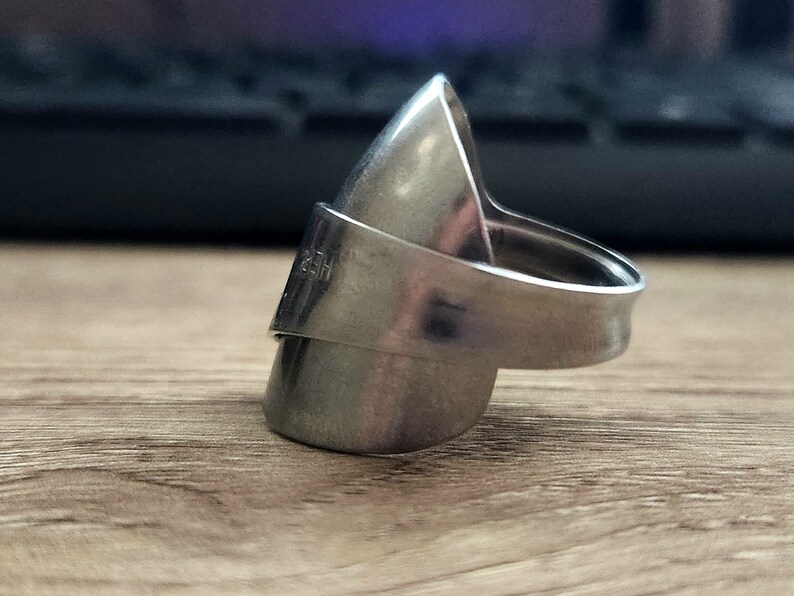 K&ouml;nnte beinhalten: Ein silberner Ring aus einem verbogenen L&ouml;ffel. Der Ring ist oval geformt und hat ein Band, das sich um den Finger legt.