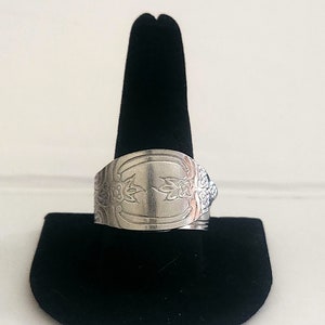 Könnte beinhalten: Ein silberner Ring aus einer wiederverwendeten Löffel mit einem floralen Design. Der Ring wird auf einem schwarzen Samtringhalter präsentiert.