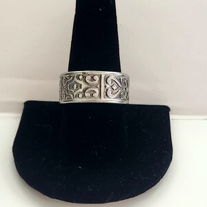 Könnte beinhalten: Ein silberner Ring mit einem komplizierten, verzierten Design. Der Ring ist breit und hat ein detailliertes Muster aus Spiralen und Herzen.