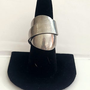 K&ouml;nnte beinhalten: Ein silberner Ring aus einem recycelten L&ouml;ffel. Der Ring ist um einen schwarzen Ringst&auml;nder gewickelt. Der L&ouml;ffel tr&auml;gt die Gravur "1.35K" und "HEAVY".