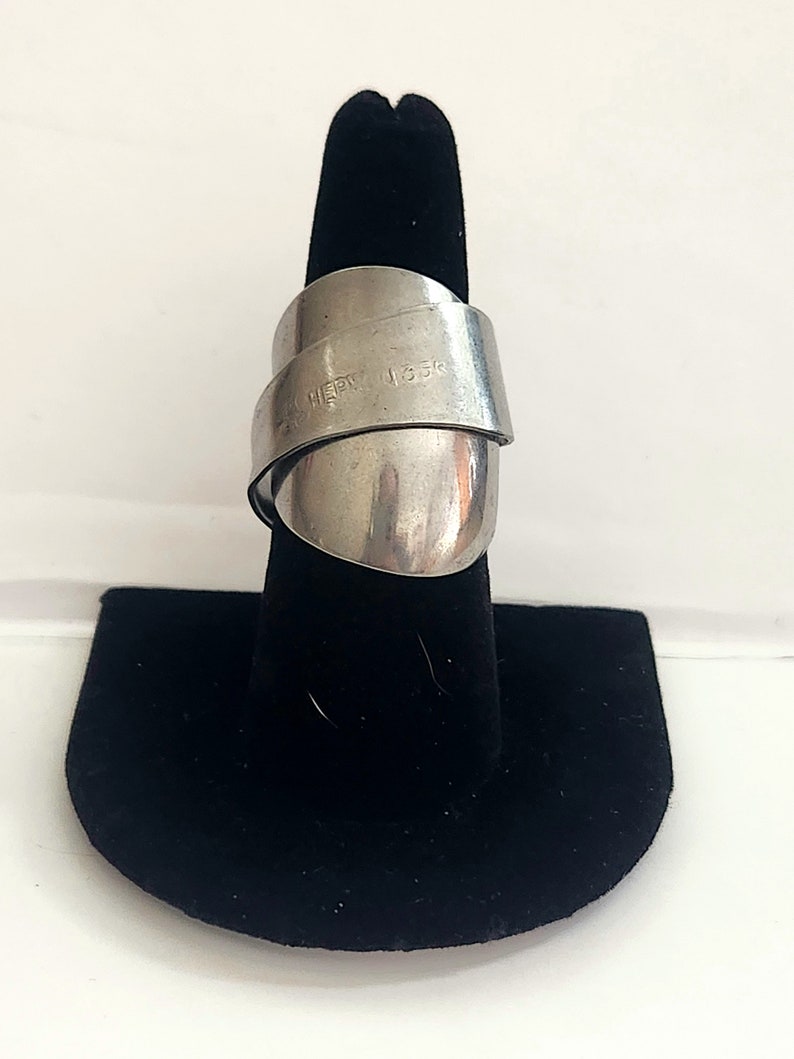 K&ouml;nnte beinhalten: Ein silberner Ring aus einem recycelten L&ouml;ffel. Der Ring ist um einen schwarzen Ringst&auml;nder gewickelt. Der L&ouml;ffel tr&auml;gt die Gravur "1.35K" und "HEAVY".