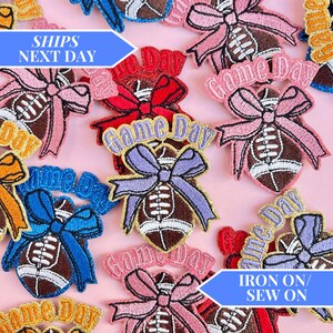 Op de afbeelding: Een set strijk- of naai-patches met een voetbal met een strik en de tekst "Game Day". De patches zijn verkrijgbaar in verschillende kleuren, waaronder roze, blauw, paars en rood.