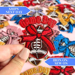 May include: A set of iron-on or sew-on patches featuring a football with a red bow and the text "Game Day". The patches are surrounded by other patches with different designs.