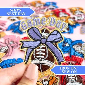 Puede incluir: Un conjunto de parches para planchar o coser que presentan un balón de fútbol con un lazo morado y el texto "game day" en purpurina dorada. Los parches son perfectos para añadir un toque divertido a la ropa, bolsos u otros accesorios.