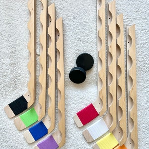 Puede incluir: Conjunto de 10 palos de hockey de madera con cinta de colores en las palas. Los palos est&aacute;n dispuestos en dos filas, la fila superior tiene cinta negra, verde, azul y morada, y la fila inferior tiene cinta roja, blanca, amarilla y naranja.