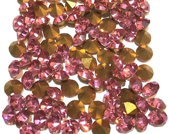 May include: A collection of pink and gold rhinestones. The rhinestones are faceted and have a shiny finish. They are scattered on a white background.