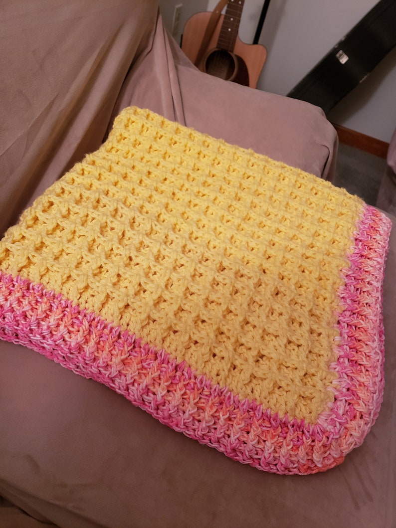 May include: A yellow crocheted baby blanket with a pink and orange crocheted border.