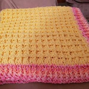 May include: A yellow crocheted baby blanket with a pink and orange crocheted border.