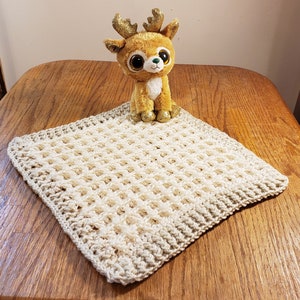 May include: A crocheted baby blanket in a cream and beige color with a waffle stitch pattern. A plush reindeer toy is sitting on top of the blanket.