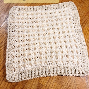 May include: A cream-colored crocheted square blanket with a textured pattern. The blanket is 12 inches by 12 inches and is labeled "Lovey 12 x 12".