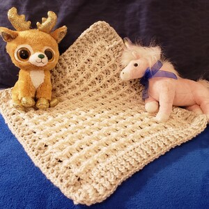May include: A beige crocheted baby blanket with a brown deer and a pink unicorn plush toy on top.