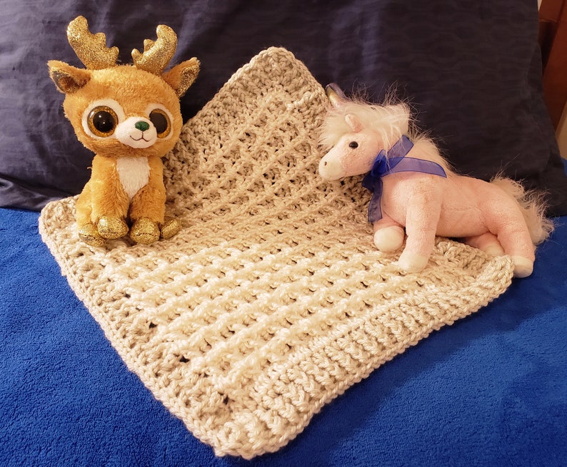 May include: A beige crocheted baby blanket with a brown deer and a pink unicorn plush toy on top.