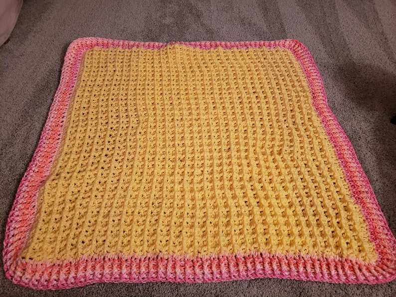 May include: A yellow crocheted blanket with a pink and orange border.