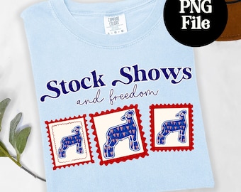 May include: Light blue t-shirt with the words "Stock Shows and freedom" in navy blue script. The shirt features three postage stamp-style images of a sheep with a red, white, and blue design. The shirt is a Comfort Colors brand.