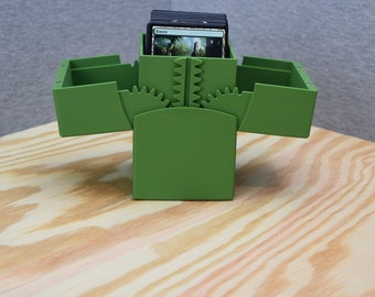 May include: A green card storage box with a deck of cards inside. The box has a gear design on the top and a hinged lid that opens to reveal the cards.