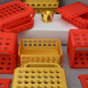 Op de afbeelding: Een set van 3D-geprinte opbergdozen in rood en goud. De dozen zijn gemaakt van plastic en hebben een rasterpatroon. De dozen zijn op elkaar gestapeld.
