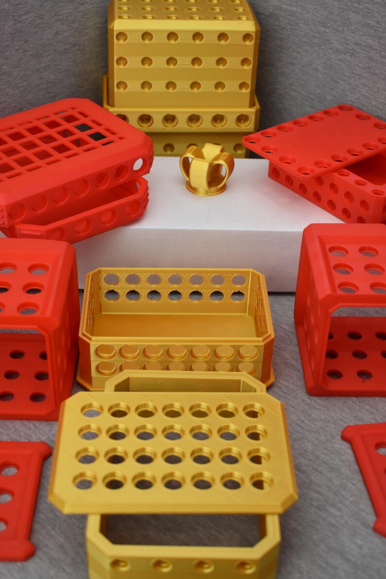 Op de afbeelding: Een set van 3D-geprinte opbergdozen in rood en goud. De dozen zijn gemaakt van plastic en hebben een rasterpatroon. De dozen zijn op elkaar gestapeld.