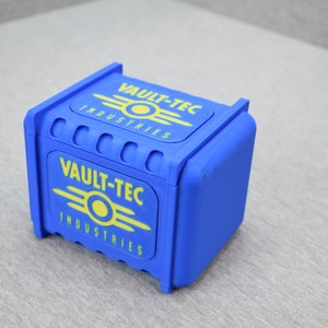 以下が含まれることがあります： 前面と上にVault-Tec Industriesのロゴが書かれた青い箱。ロゴは黄色で、スタイリッシュな原子記号が描かれている。
