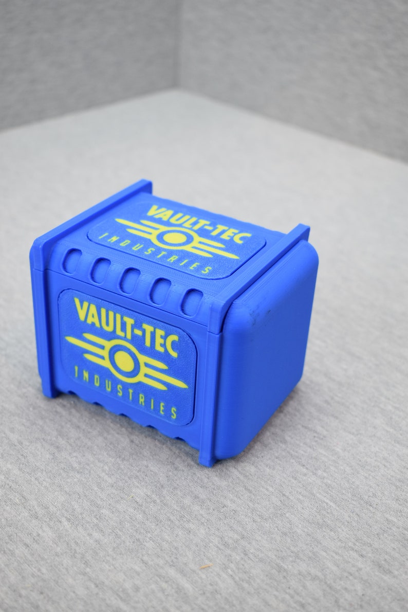 以下が含まれることがあります： 前面と上にVault-Tec Industriesのロゴが書かれた青い箱。ロゴは黄色で、スタイリッシュな原子記号が描かれている。