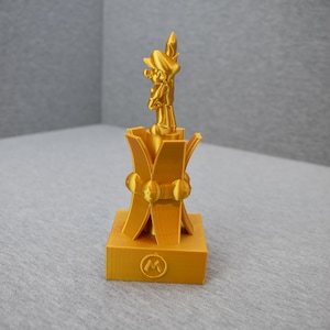 May include: A gold-colored 3D printed trophy featuring a character from the Super Mario franchise standing on a base with a stylized "M" logo.