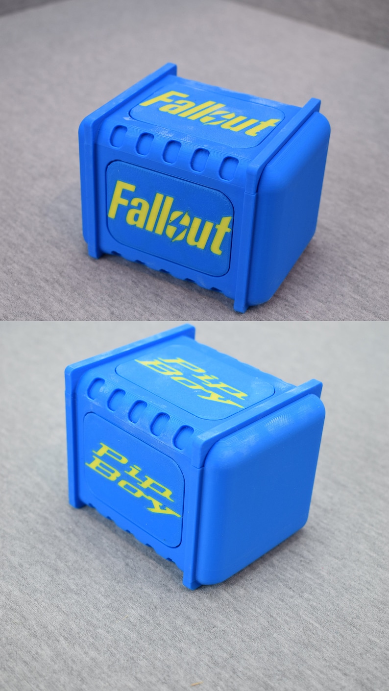 以下が含まれることがあります： 上面が黄色い「Fallout」ロゴ、側面が黄色い「Pip-Boy」ロゴの青いプラスチック製の箱です。