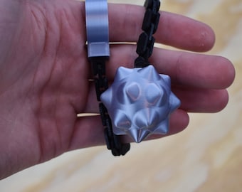 May include: A silver-coloured, spiked mace pendant with a black chain and a silver clasp. The mace is held in a hand against a light wood grain background. The pendant is a unique accessory.