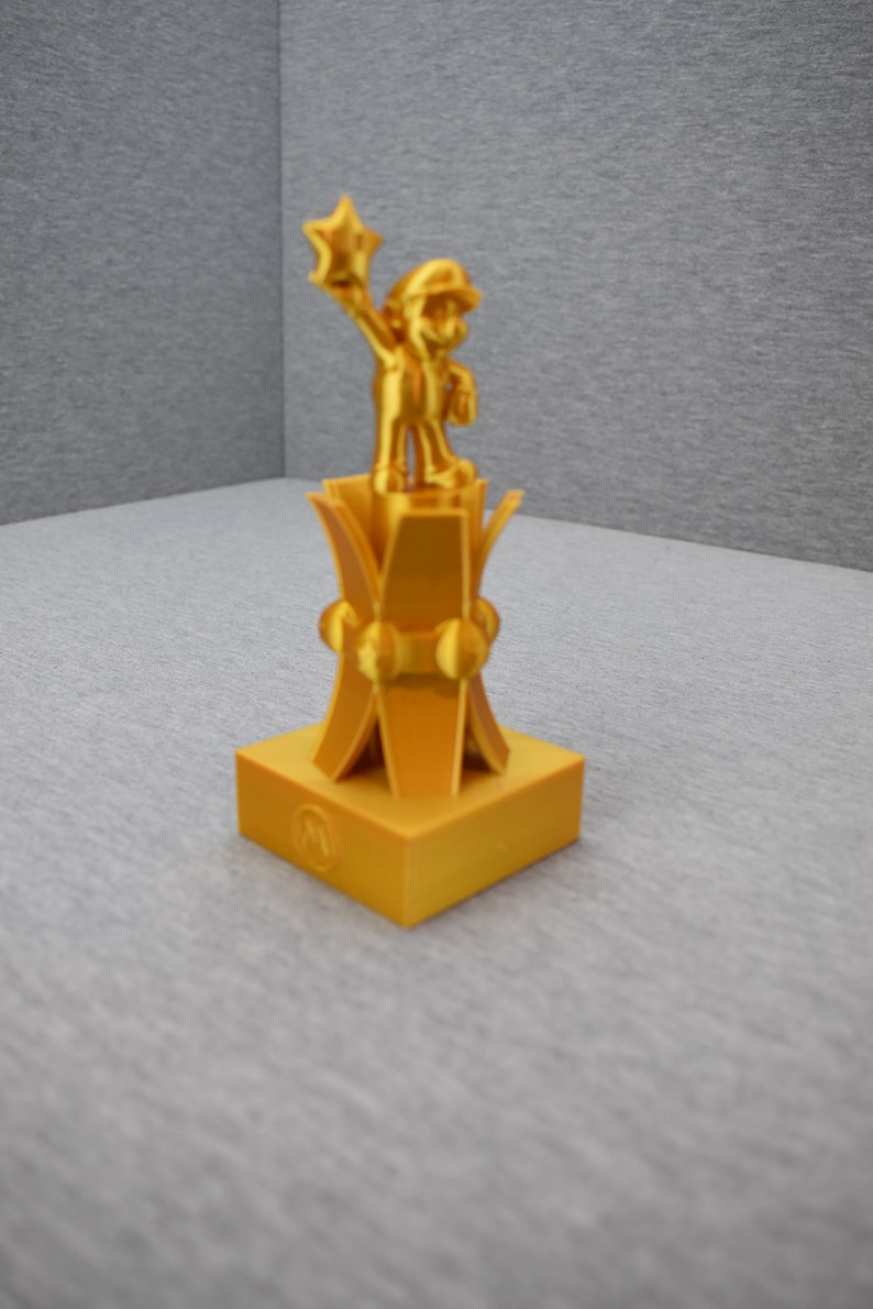 May include: A gold-colored trophy featuring a figurine of a video game character holding a star. The character is standing on a pedestal with a circular base.