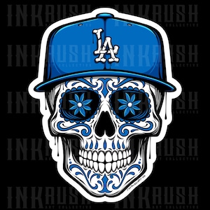 May include: A white sugar skull with blue floral details wearing a blue baseball cap with the letter "L" and "A" on the front. The skull has a white background and a blue outline.