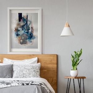 May include: A white framed abstract painting with blue, brown, and white colours hangs above a wooden headboard with a white and grey patterned bedspread. A white pendant light hangs from the ceiling above a small wooden side table with a white planter and a green plant.