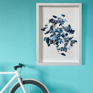 May include: A white framed picture with a blue and white abstract art print. The art print is a collage of different shapes and textures.