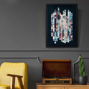 May include: A framed abstract art print with a black frame and a colourful geometric design. The print is made up of many small squares of different colours, including blue, green, red, and white. The print is hanging on a grey wall.