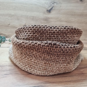 Könnte beinhalten: Ein handgehäkelter Schal in Brauntönen, von hellem Beige bis dunkler Schokolade. Das strukturierte Strickwerk ist gefaltet und zeigt die Innen- und Außenfarben. Der Halswärmer wird auf einer Holzoberfläche präsentiert.