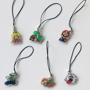 Puede incluir: Seis coloridos colgantes acrílicos con personajes de la serie de videojuegos Super Mario. Cada colgante tiene un cordón negro y un cierre de metal plateado. Los personajes incluyen a Mario, Luigi, la Princesa Peach, Yoshi, Bowser y un fantasma Boo.