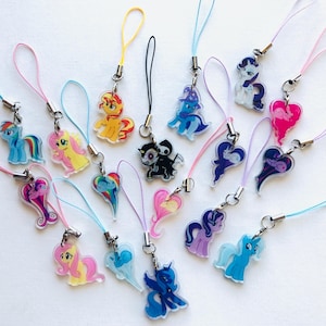 Peut inclure: Une collection de breloques en acrylique représentant divers personnages de poneys de dessin animé et une figure de faucheuse, chacune attachée à une boucle en cordon de nylon coloré. Les breloques présentent des couleurs variées dont bleu, jaune, rose et violet.