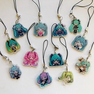 May include: A selection of anime-style acrylic charms, each depicting a different character with vibrant hair and clothing. The charms are attached to black lanyards with silver-coloured clasps. The items are presented on a white surface.