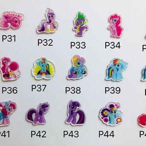 May include: A set of 15 colorful My Little Pony character charms. The charms are made of clear plastic with a printed image of a pony on each one. The charms are numbered P31 through P45.