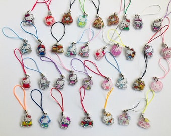 May include: A collection of colourful Hello Kitty charms with various designs, including a fire engine, a house, a car, and a cat. The charms are attached to strings and are perfect for adding a touch of whimsy to your keys, bags, or phone.