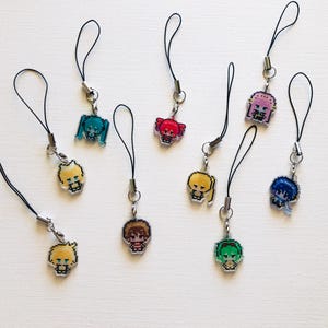 May include: A collection of nine pixel art character charms, each attached to a black cord loop. The charms feature various figures with distinct hair colors including teal, red, yellow, pink, blue, brown, and green, rendered in a blocky style.
