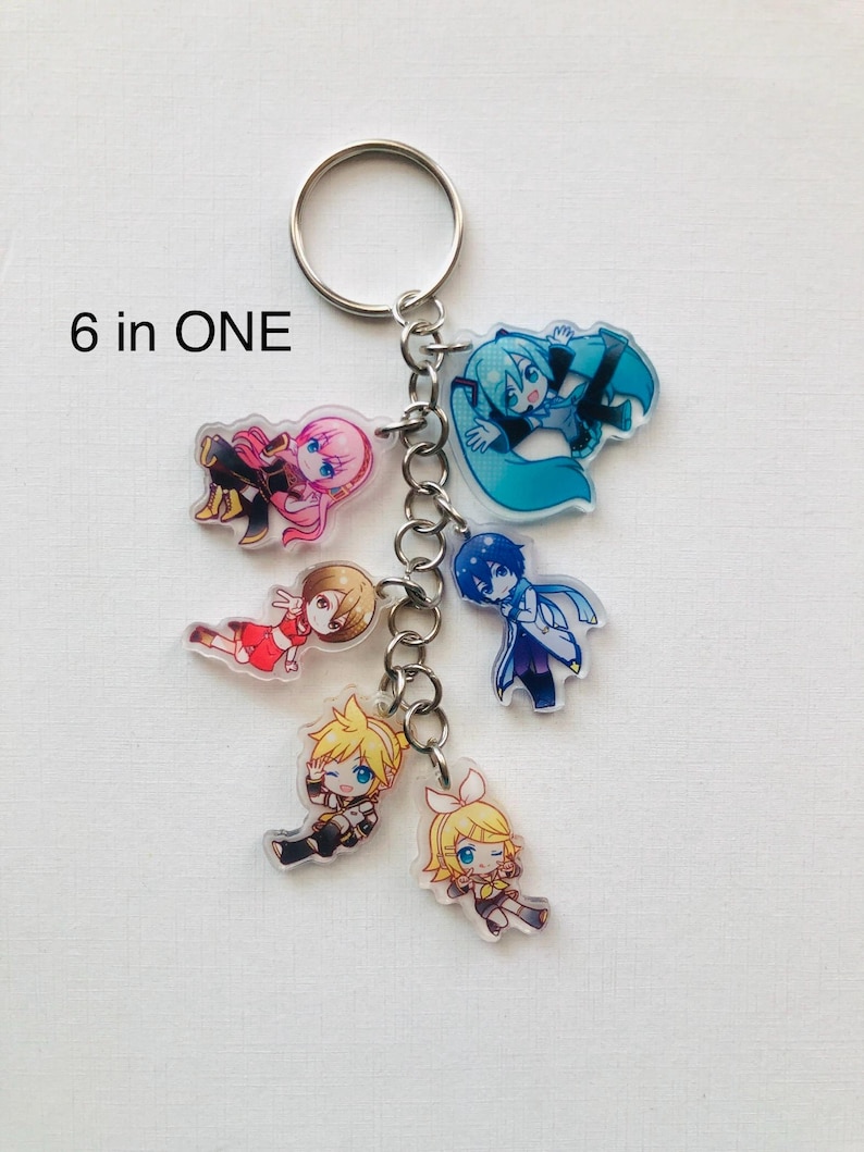 Peut inclure: Un porte-cl&eacute;s avec six breloques de personnages de style anime. Chaque breloque repr&eacute;sente un personnage diff&eacute;rent avec des couleurs de cheveux et de v&ecirc;tements distinctes. Les breloques sont reli&eacute;es par une cha&icirc;ne argent&eacute;e et un porte-cl&eacute;s. Le texte "6 in ONE" est imprim&eacute; en haut &agrave; gauche.